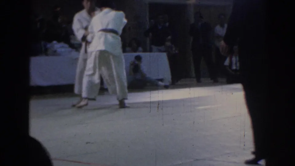 Two competitors in white judogi continue a standing exchange on a light mat in the Los Angeles judo venue.