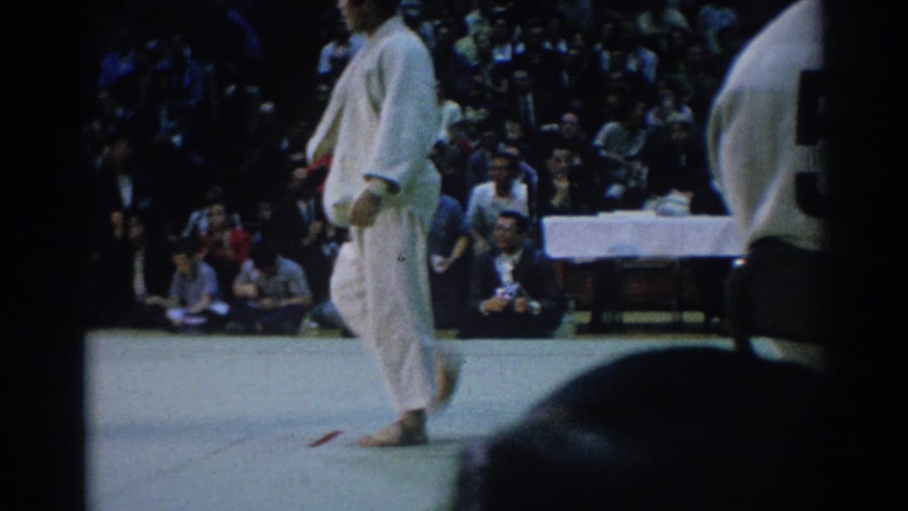 A competitor in a white judogi walks across the mat as the crowd watches from the edge of the 1967 Los Angeles venue.