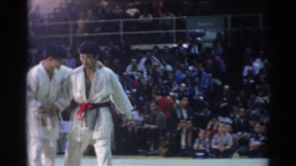 In 1967 Los Angeles footage, two martial arts competitors in white gi face each other on an indoor mat before crowded bleachers.