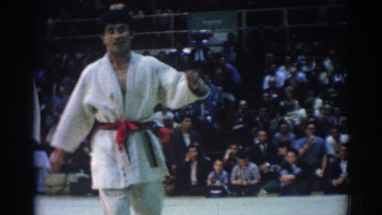 A competitor in a white gi and red and black belt moves across the mat in 1967 Los Angeles indoor competition footage.