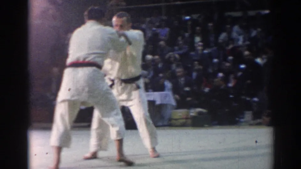 1967 Los Angeles judo match frame with two male competitors facing each other on a gym mat before a large audience.
