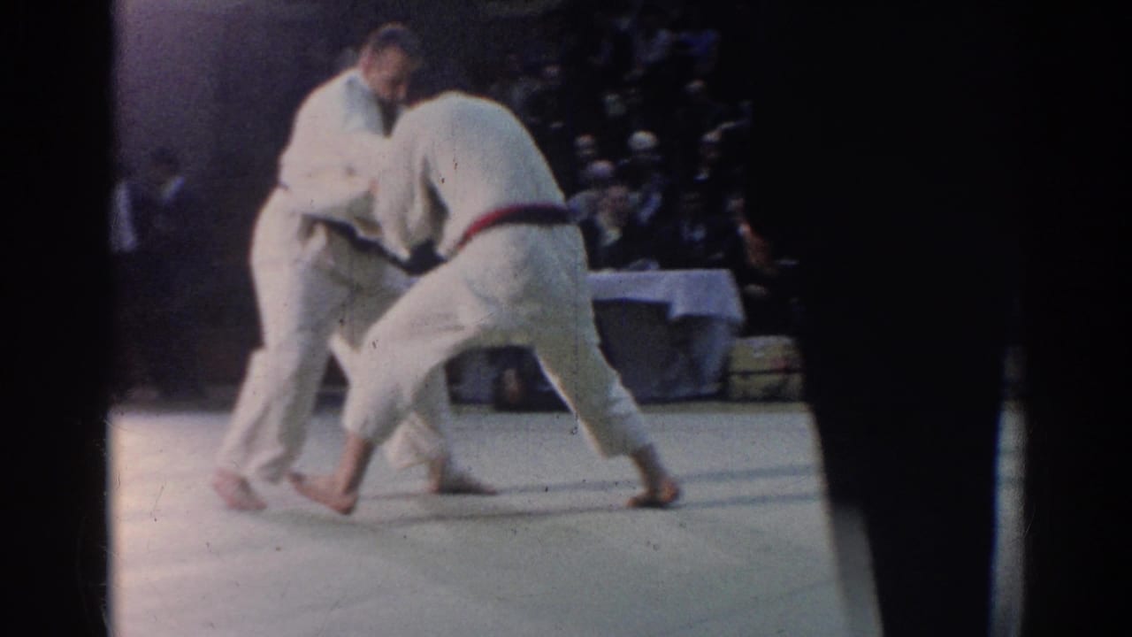 1967 Los Angeles 8mm frame showing two male judo competitors grappling on a mat while an official stands near the edge.