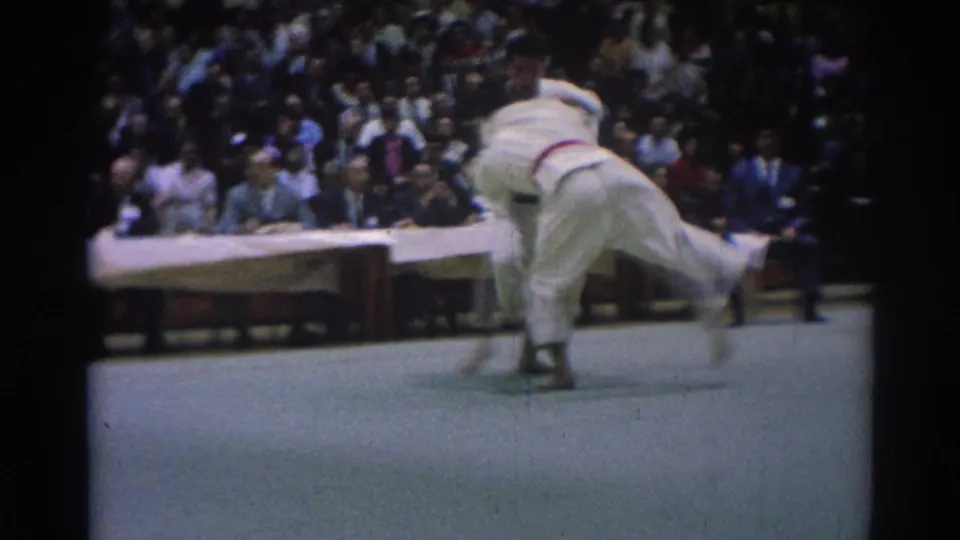 A 1967 tournament frame captures a karate competitor being pulled off balance during a throw attempt on the mat.