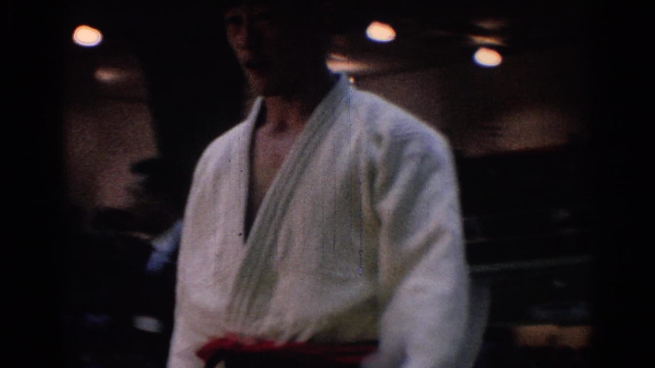 Judo competitor in a white gi and red belt standing under dim indoor lights.