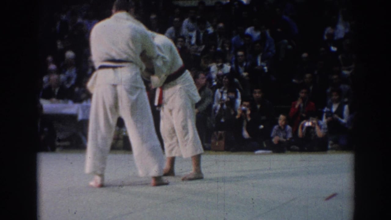 Two men in white judo uniforms hold a standing grip during the 1967 Los Angeles match, with spectators and cameras behind them.