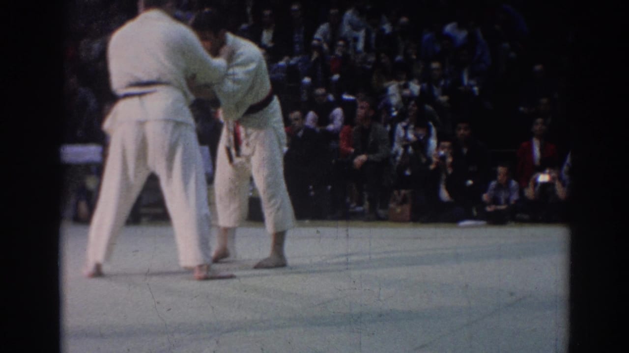 The match returns to an upright grip, showing two barefoot competitors in white uniforms before spectators in 1967 Los Angeles footage.
