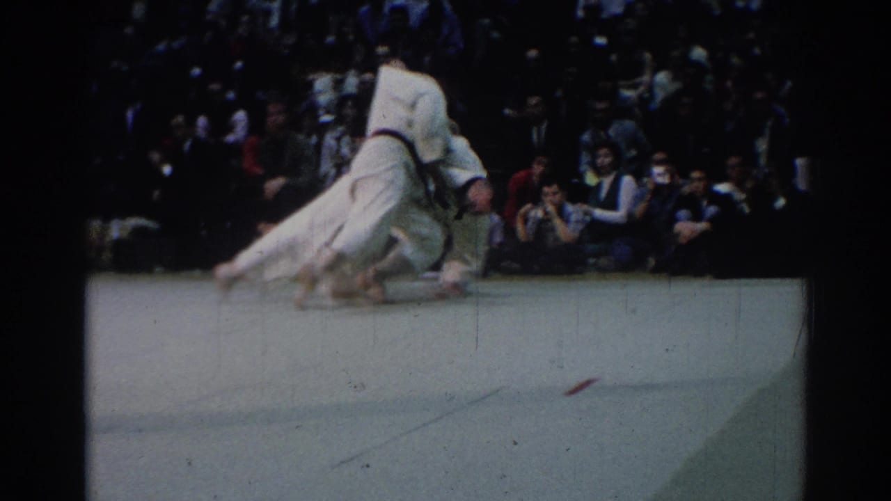 During the 1967 Los Angeles judo match, one athlete is lifted and thrown as the audience watches from behind the competition area.