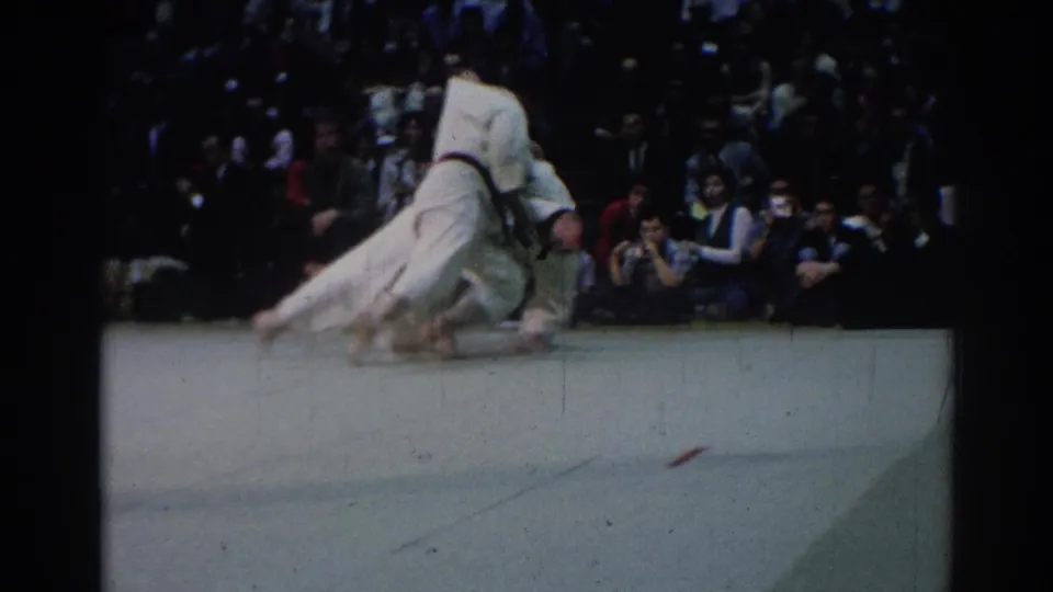 During the 1967 Los Angeles judo match, one athlete is lifted and thrown as the audience watches from behind the competition area.