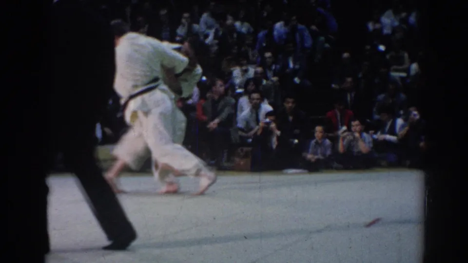 At the end of the 1967 Los Angeles clip, the judo competitors move together across the mat while an official passes in front of the camera.
