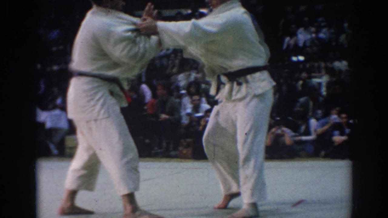 The competitors grip each other's gi during a judo-style exchange, filmed from the audience area in 1967 Los Angeles.