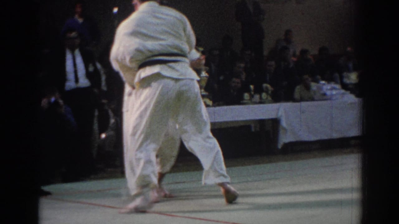 The bout is seen from behind one athlete in a white gi as the competitors move across the mat in the Los Angeles venue.