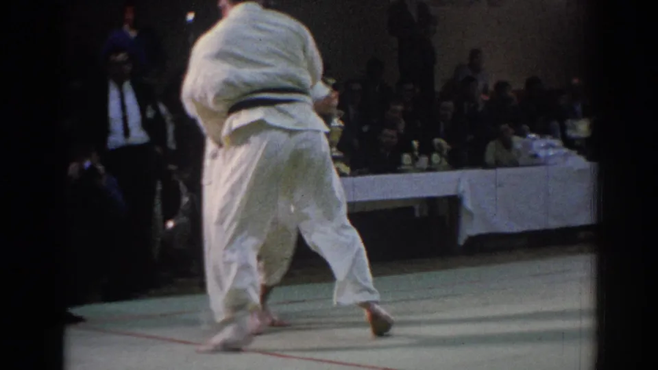 The bout is seen from behind one athlete in a white gi as the competitors move across the mat in the Los Angeles venue.