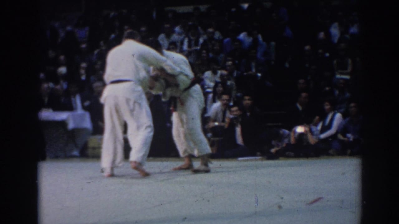 1967 Los Angeles 8mm frame showing two judo athletes in white uniforms maintaining grips during an indoor competition.