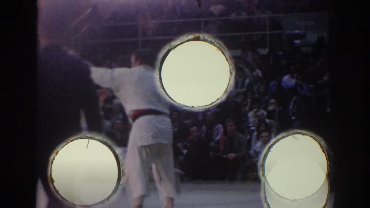 1967 Los Angeles arena view with a judo athlete in a white gi, bright lamps, and spectators behind the mat.
