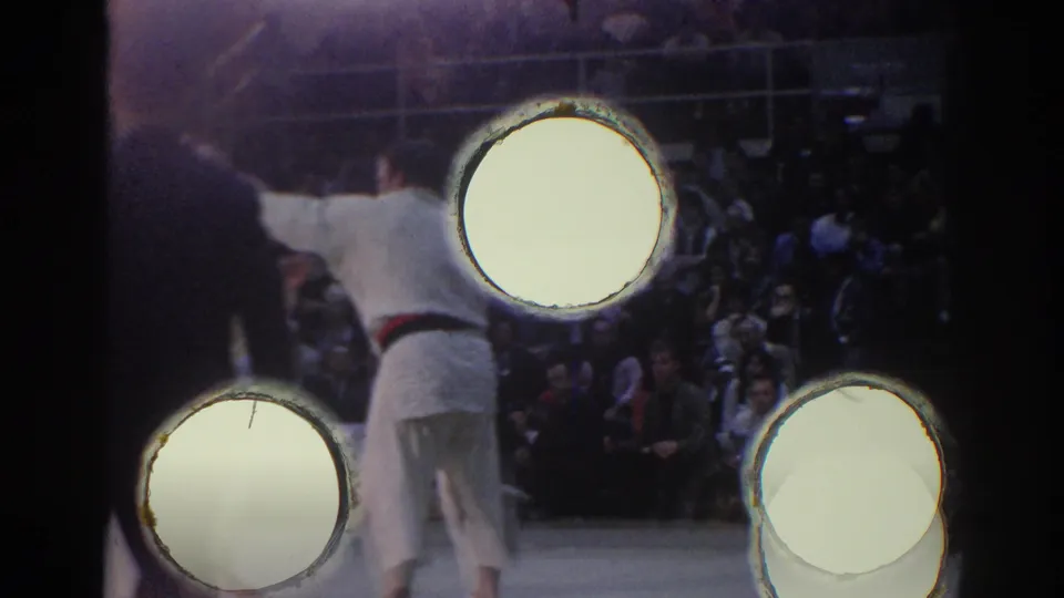 1967 Los Angeles arena view with a judo athlete in a white gi, bright lamps, and spectators behind the mat.