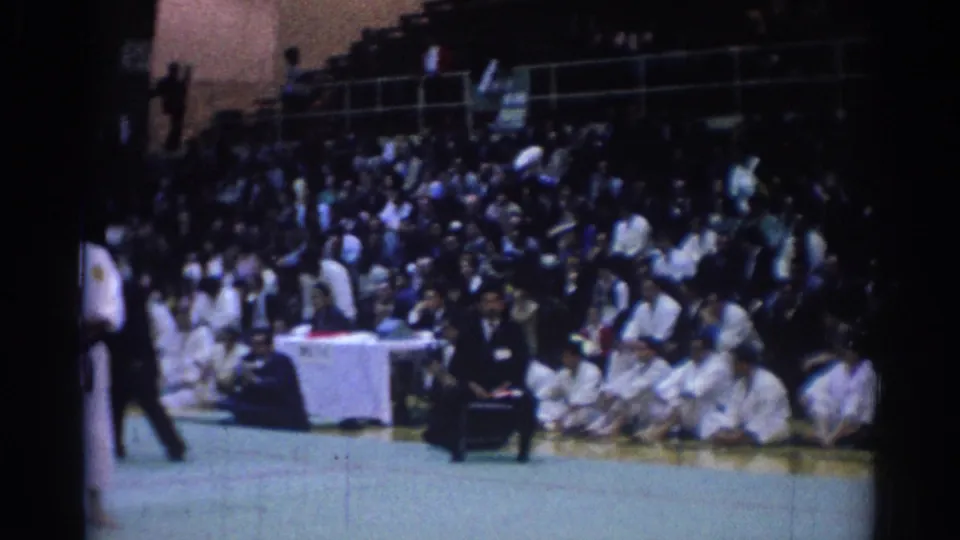 1967 Los Angeles tournament footage showing spectators in bleachers behind a judges' table at the edge of a martial arts mat.