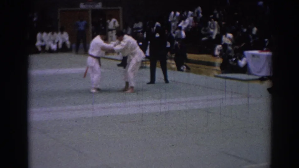 1967 Los Angeles 8mm footage frame showing two competitors in white gi gripping each other on a green tournament mat.
