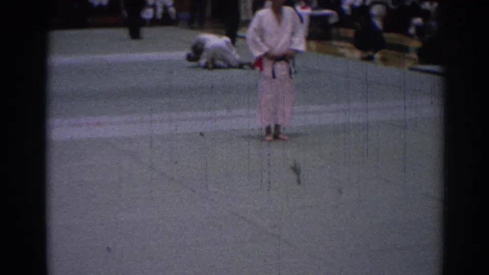 1967 Los Angeles judo scene with a black-belt competitor standing on the mat as another fighter remains on the ground in the background.