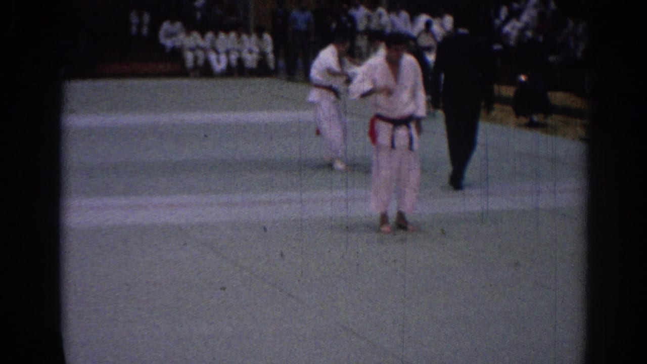 1967 Los Angeles tournament frame with a gi-clad competitor in front, another pair behind, and a referee near the mat edge.