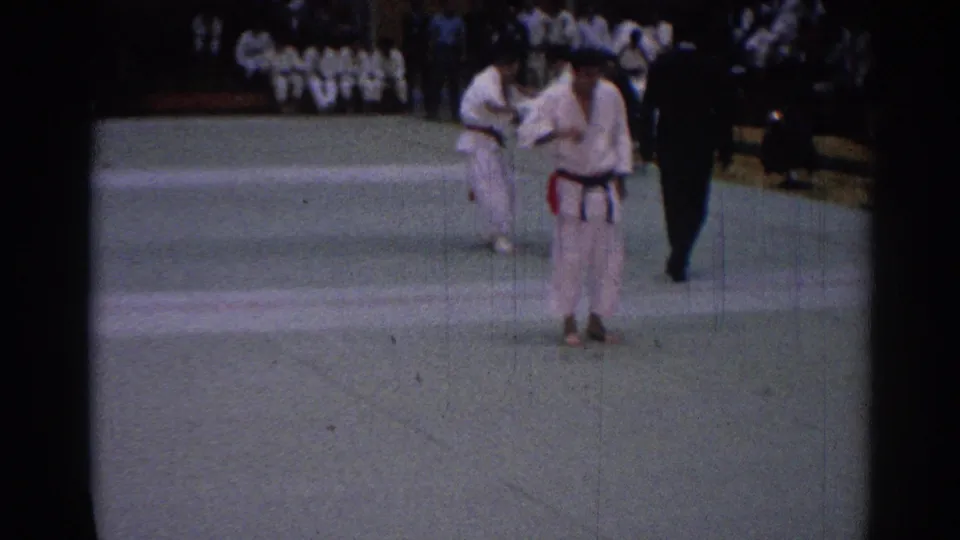 1967 Los Angeles tournament frame with a gi-clad competitor in front, another pair behind, and a referee near the mat edge.