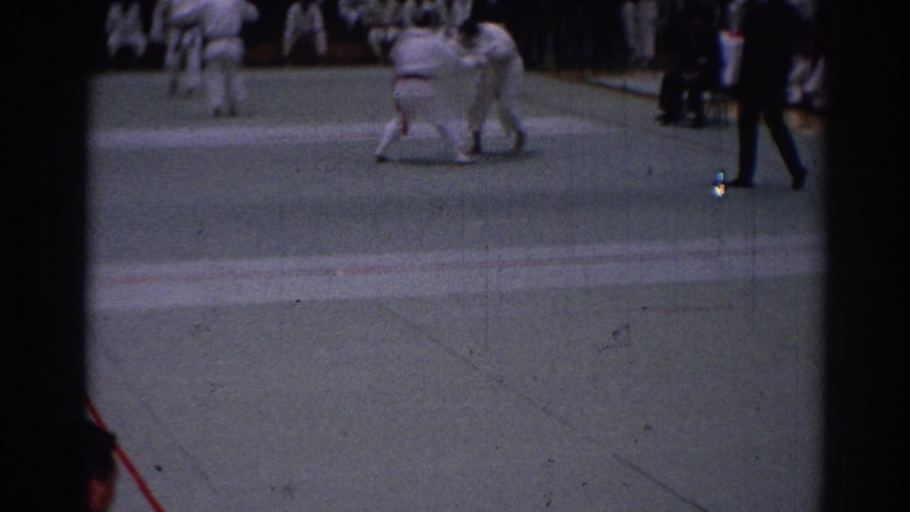 1967 Los Angeles karate tournament frame with two gi-clad competitors grappling and a referee moving along the right edge.