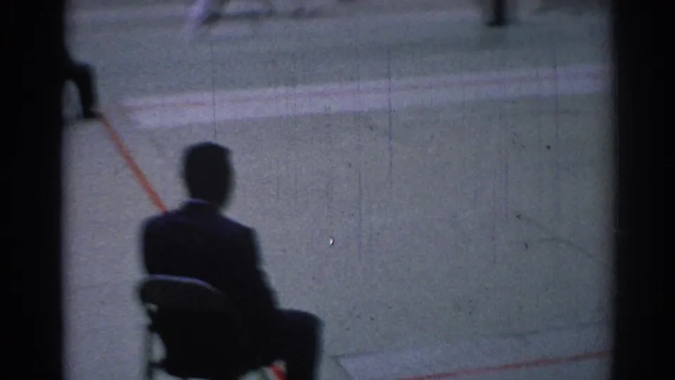 1967 Los Angeles 8mm frame with a seated foreground figure watching blurred karate action across the green mat.
