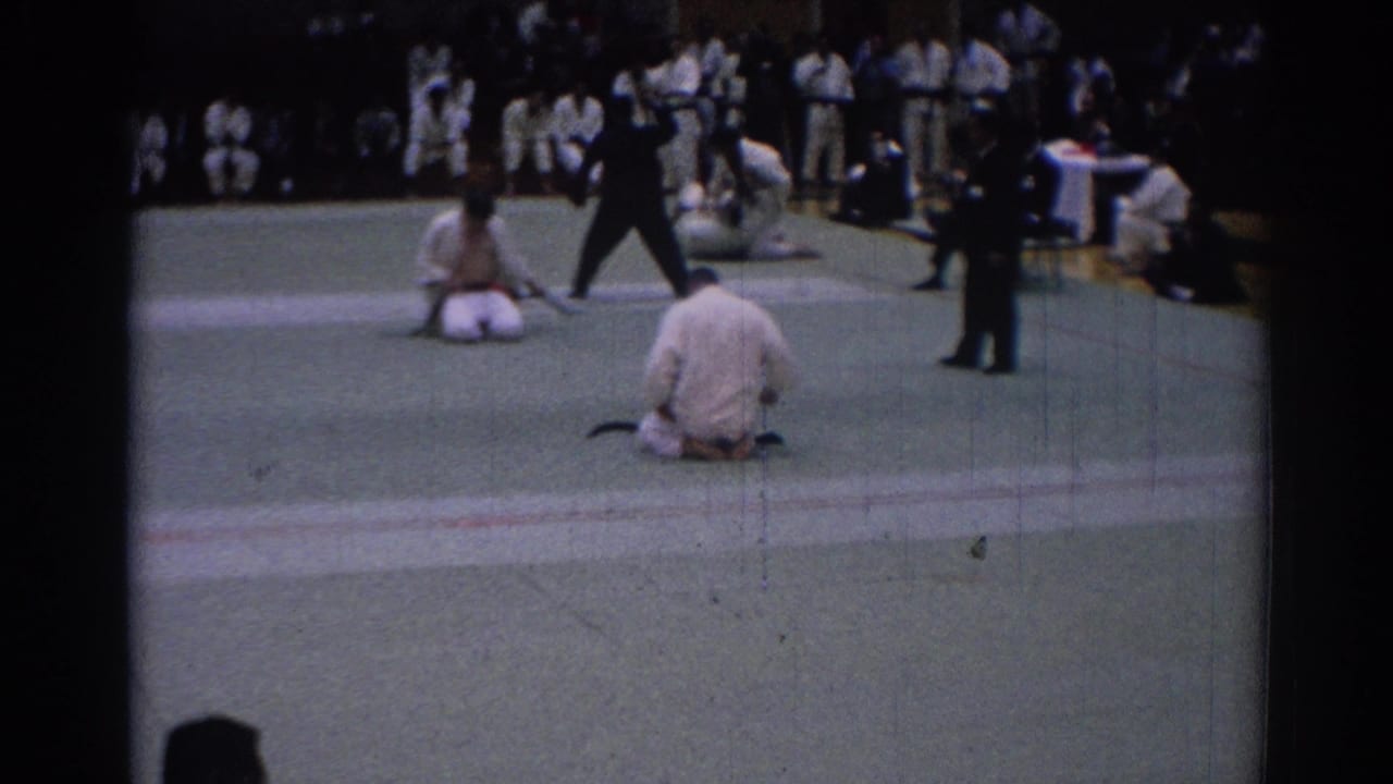 Indoor Los Angeles karate tournament scene from 1967 with kneeling competitors, officials, and spectators around the mat.