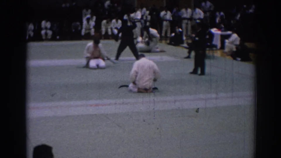 Indoor Los Angeles karate tournament scene from 1967 with kneeling competitors, officials, and spectators around the mat.