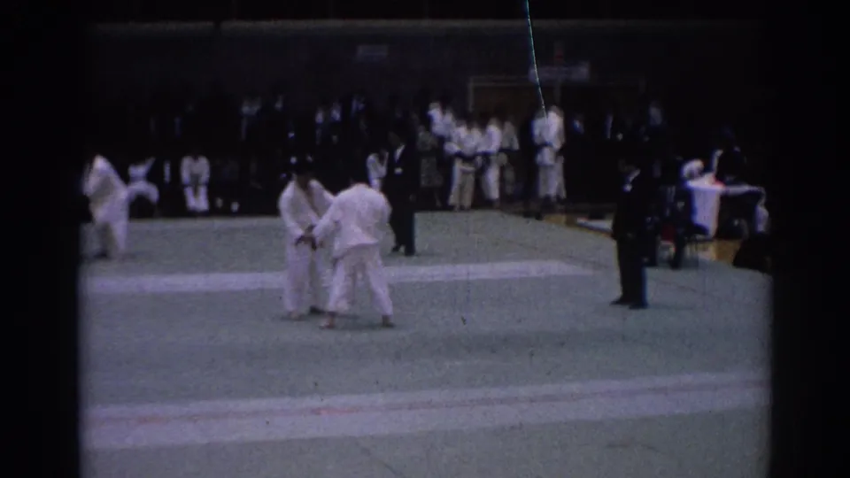 1967 Los Angeles 8mm footage frame of two karate competitors beginning an exchange on a gymnasium mat.