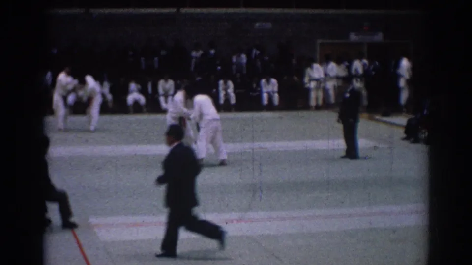 Man in a dark suit crosses the foreground during a 1967 Los Angeles karate match filmed on 8mm.
