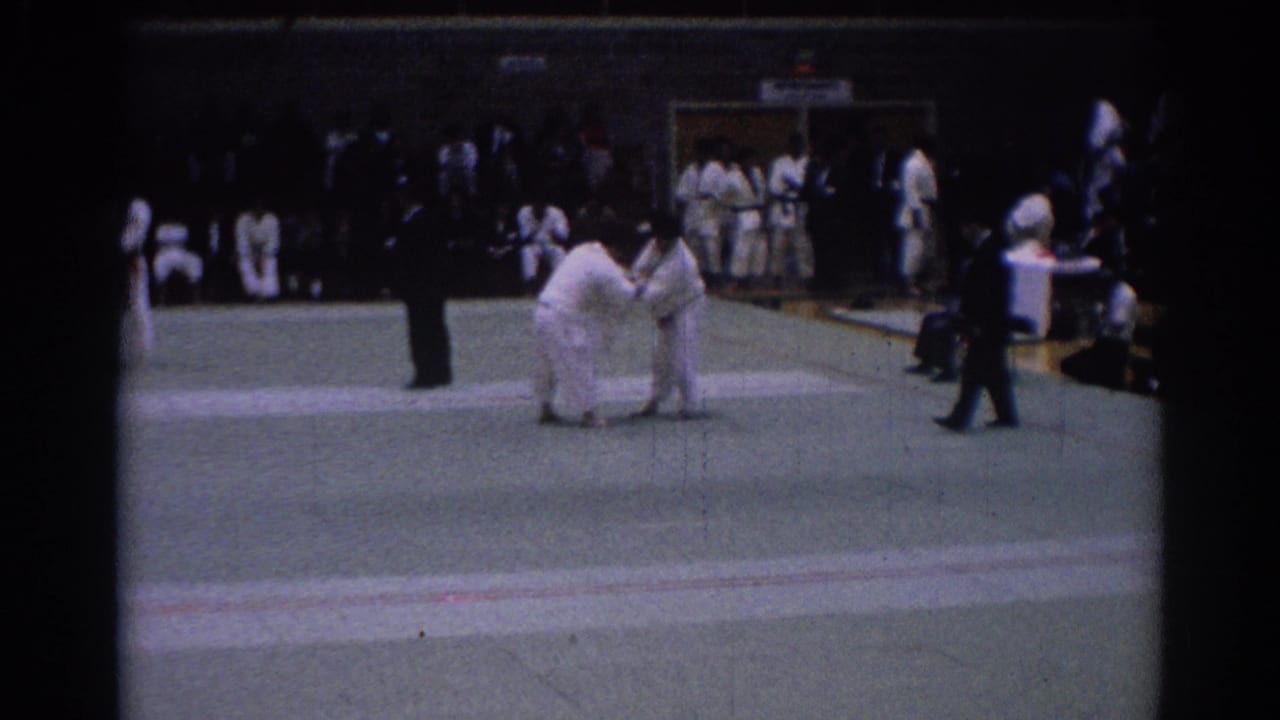 1967 Los Angeles judo tournament frame showing two white-gi competitors facing off, with a referee and several participants visible around the mat.