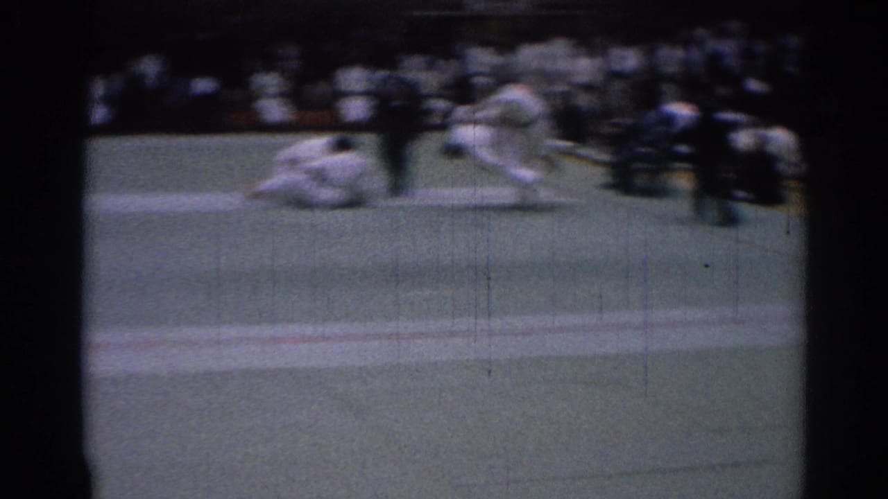 A blurred 8mm frame shows one martial arts competitor on the mat while another moves away during the bout.