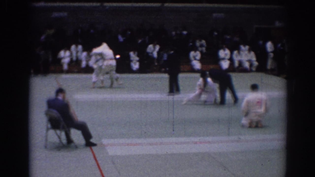 A 1967 Los Angeles karate tournament scene shows competitors on the mat, a seated judge, referees, and waiting participants in white gi.