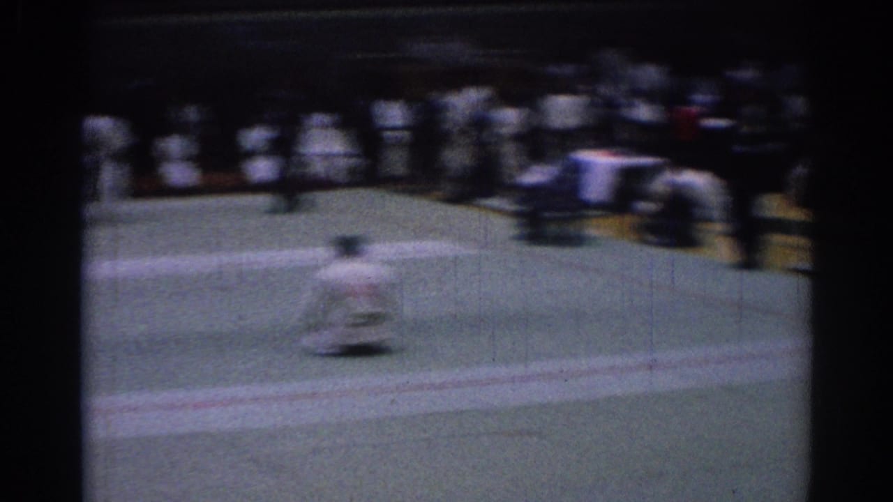 Motion-blurred 8mm frame from a Los Angeles karate competition showing a competitor moving across the mat before seated onlookers.