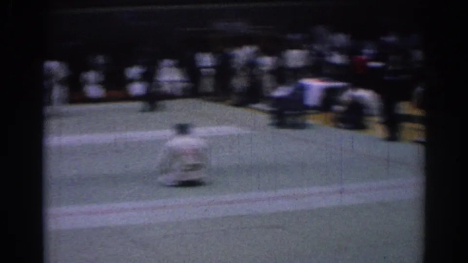 Motion-blurred 8mm frame from a Los Angeles karate competition showing a competitor moving across the mat before seated onlookers.