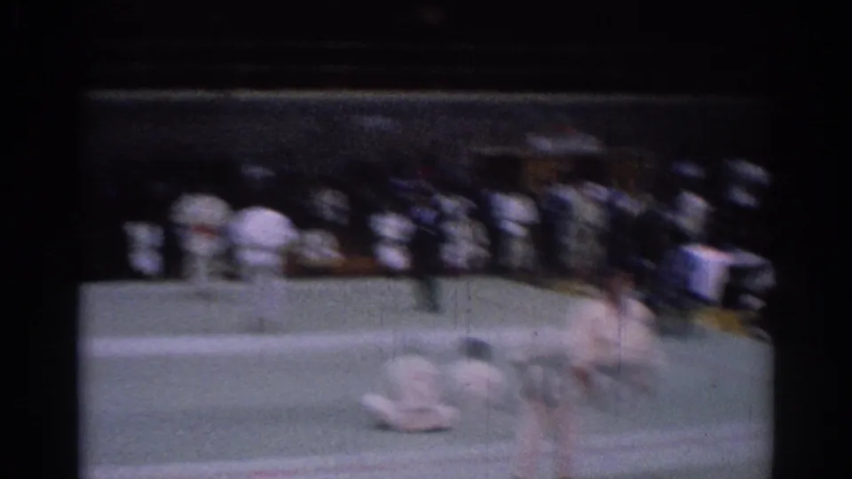 Motion-blurred 8mm frame from the 1967 Los Angeles karate tournament, with a fighter moving across the mat before seated spectators.