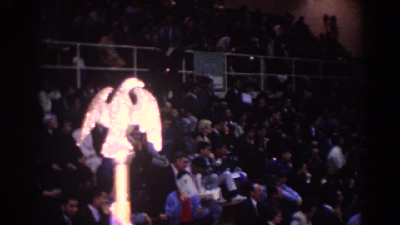 1967 Los Angeles frame with a glowing gold eagle-like symbol in front of crowded indoor seating during a martial arts event.