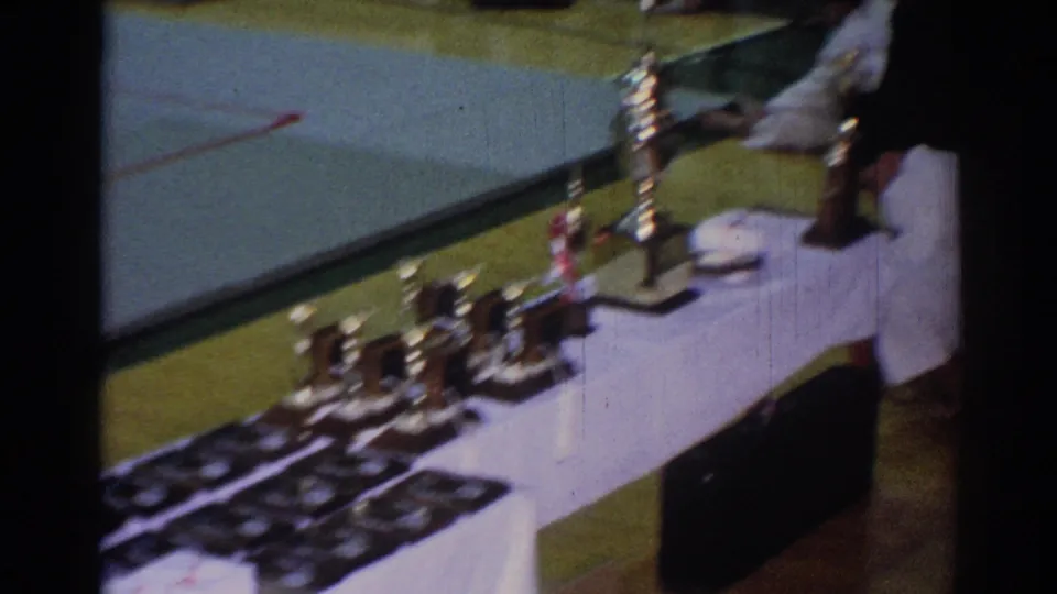 1967 Los Angeles home-movie frame showing a white-draped awards table with trophies, plaques, and a person in a gi nearby.