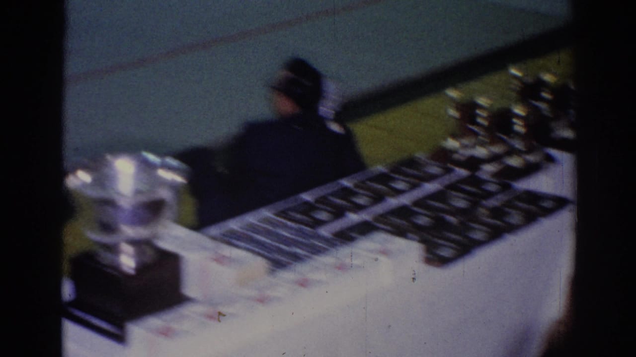 A suited man stands or moves beside the awards display, with trophies and plaques visible on the white-draped table.
