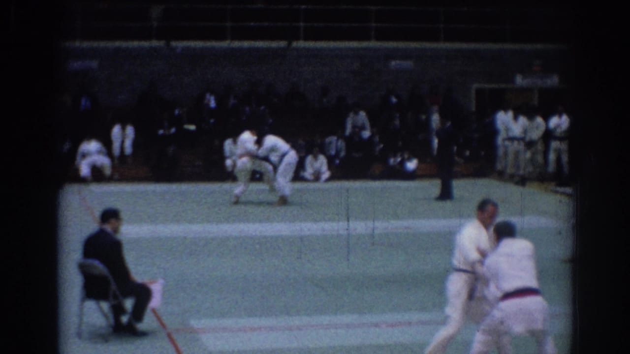 1967 Los Angeles judo match on 8mm film, with athletes in white gi grappling on a green mat before spectators.