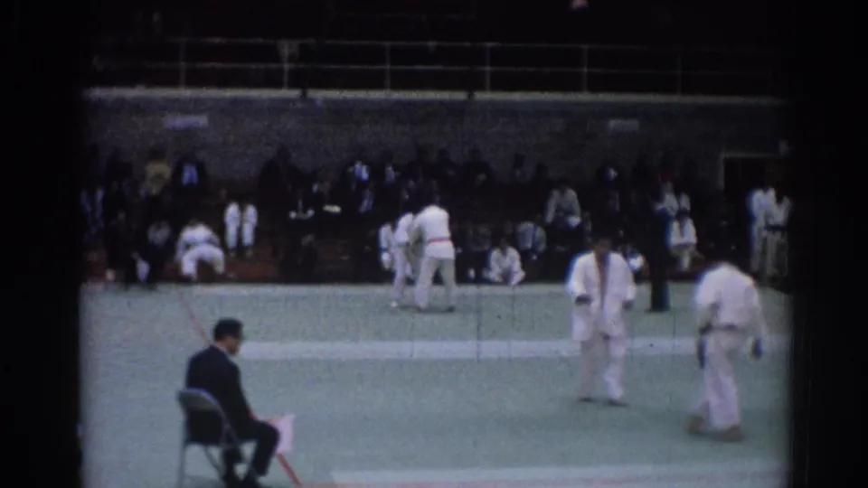 1967 Los Angeles indoor judo footage showing athletes in white gi between exchanges on a green competition mat.