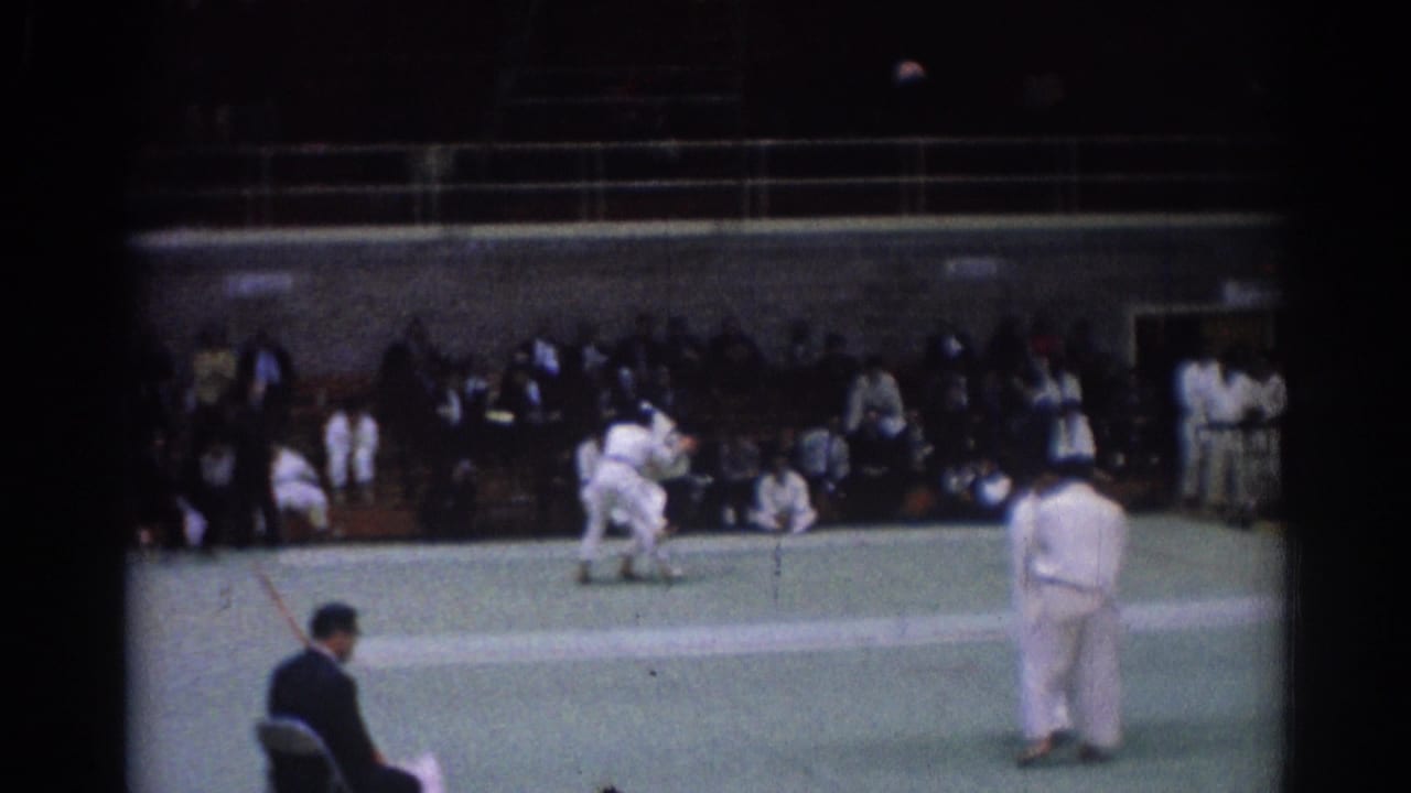 1967 Los Angeles judo championship footage with athletes grappling low on a green mat and spectators in the background.