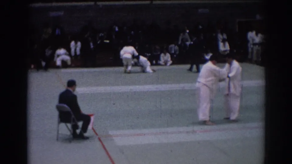 1967 Los Angeles judo competition frame with two athletes in white gi facing each other near a seated referee.