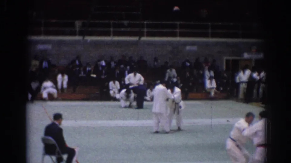 Indoor 1967 judo competition in Los Angeles, showing athletes in white gi, a referee nearby, and spectators along the far wall.