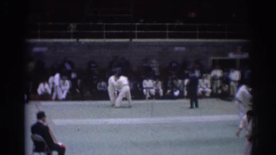 Home-movie frame from the 1967 Los Angeles judo competition, showing competitors on the mat and observers around the arena.