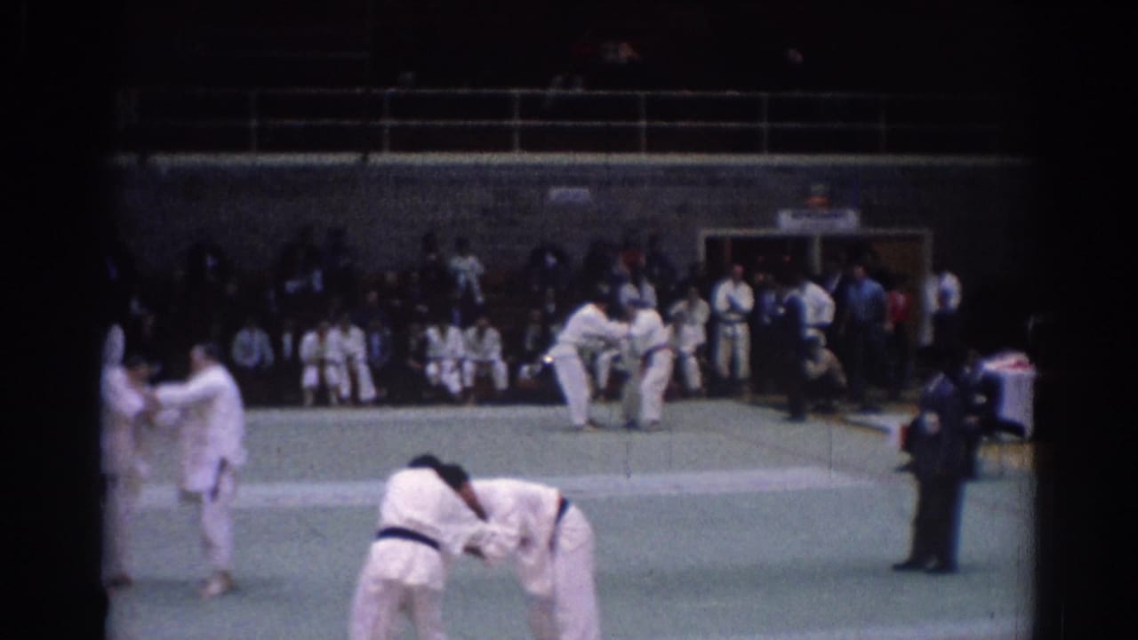1967 Los Angeles 8mm frame with multiple martial artists on a green mat, including foreground competitors and background matches.