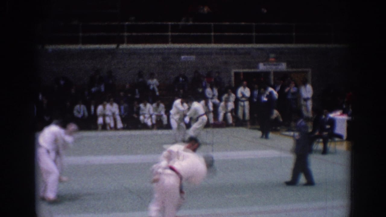 1967 Los Angeles martial arts scene with foreground grappling, a second sparring pair, a referee, and spectators along the wall.