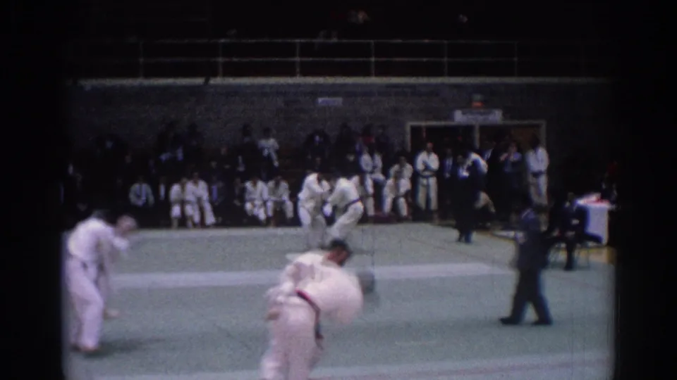 1967 Los Angeles martial arts scene with foreground grappling, a second sparring pair, a referee, and spectators along the wall.