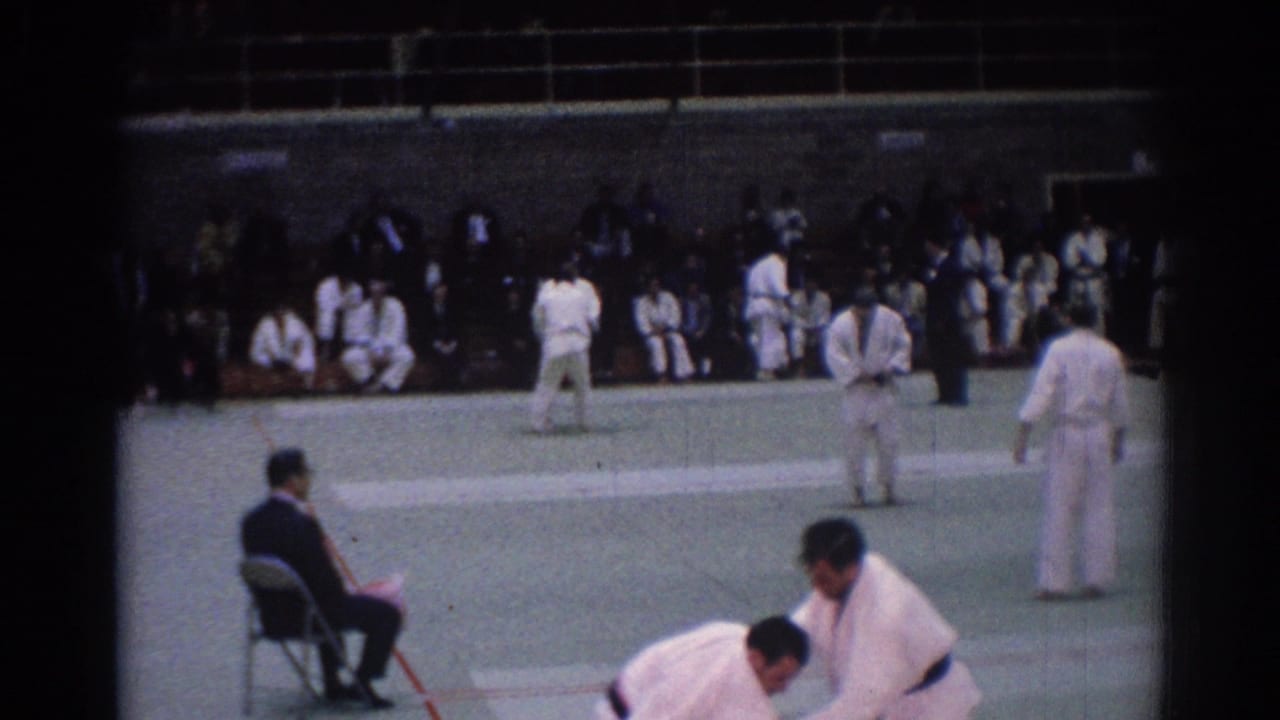 A 1967 Los Angeles judo match continues on a green mat, with a seated official and spectators visible around the gym.
