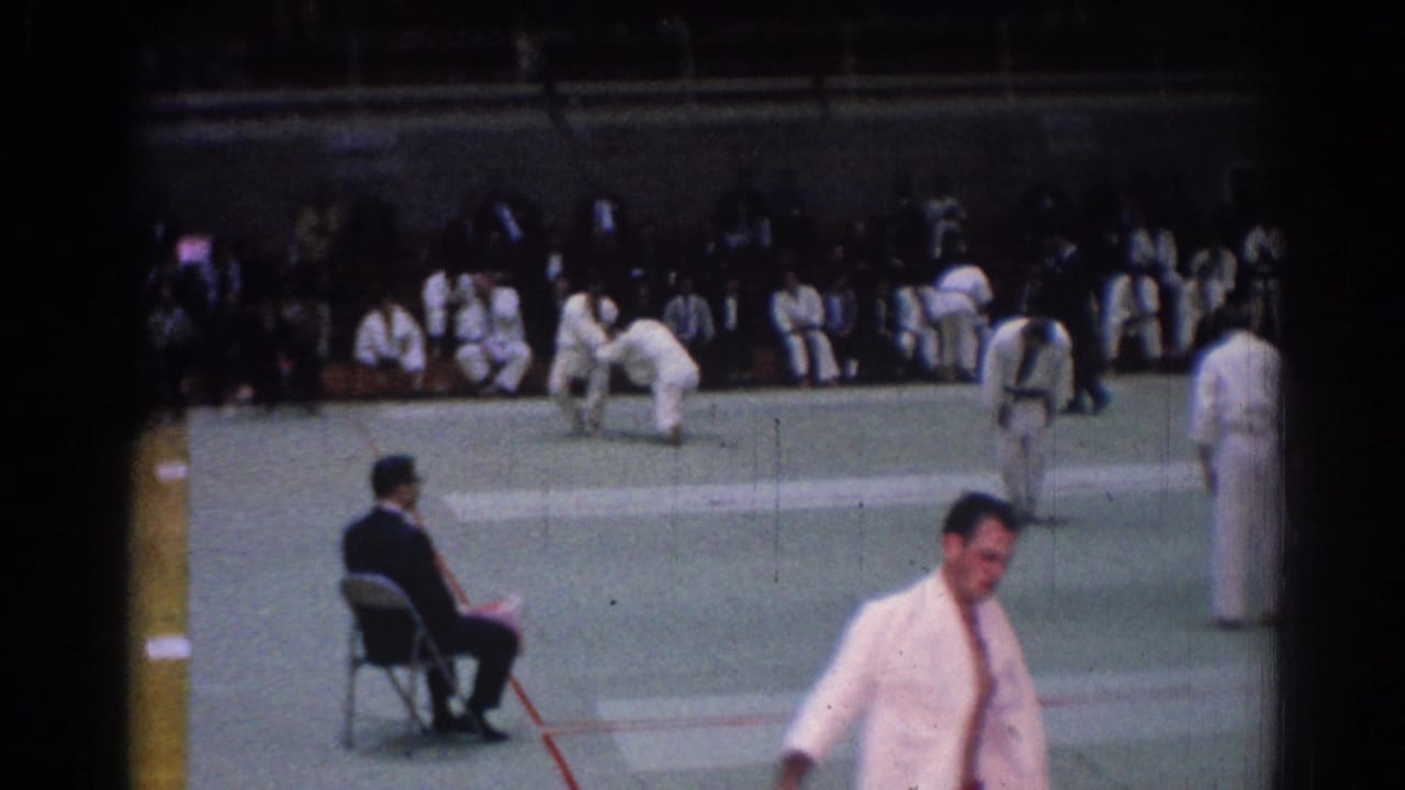 Home-movie frame from a 1967 Los Angeles judo competition, showing a competitor near the camera and spectators seated beyond the mat.